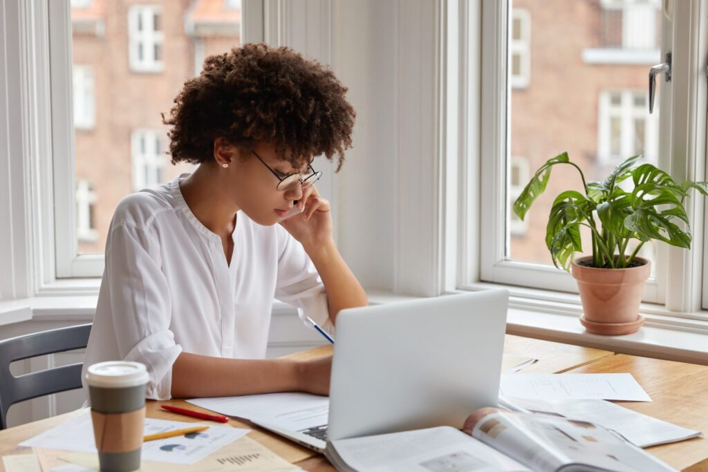 mulher negra freelancer sentada em uma mesa olhando seu notbook e calculando quanto por seu trabalho